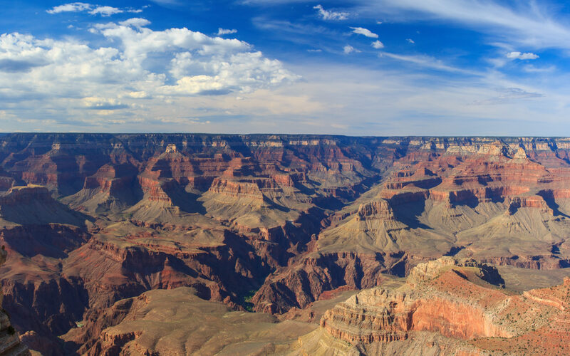 Panoramic view of the Grand Canyon from the South Rim showing layered red rock formations under blue sky with clouds