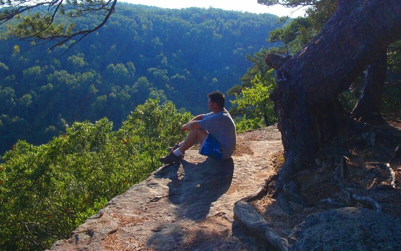 Hiker overlooking forested Ozark Mountain ridges from a rocky bluff in Arkansas