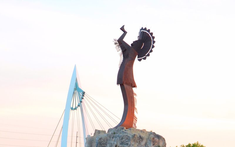 Keeper of the Plains statue at sunset in Wichita Kansas with pedestrian bridge in background