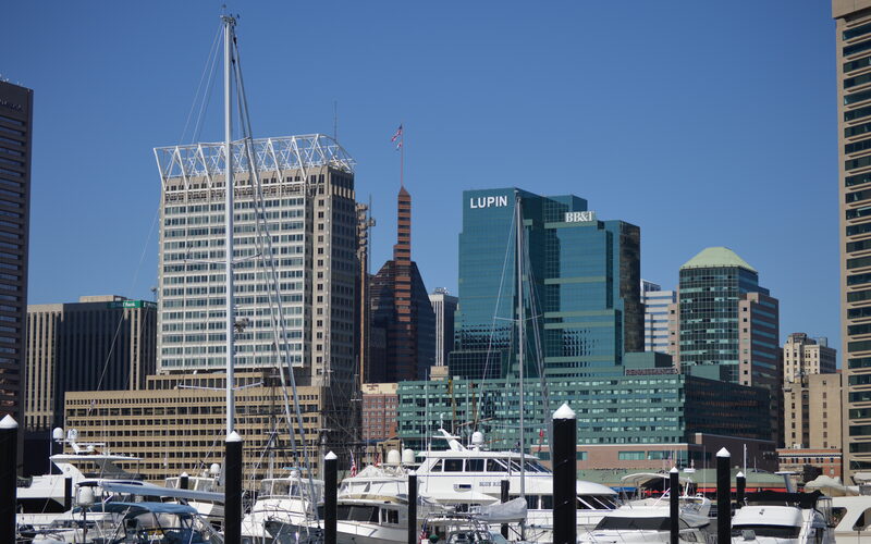 Baltimore Inner Harbor skyline with boats and yachts in the foreground and modern office towers against a clear blue sky