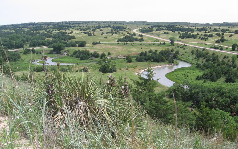 Nebraska Sandhills landscape with winding river, grass-covered rolling dunes, and native vegetation