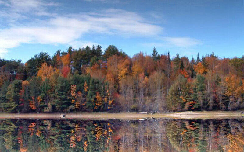 New Hampshire lake reflecting vibrant autumn foliage under a blue sky